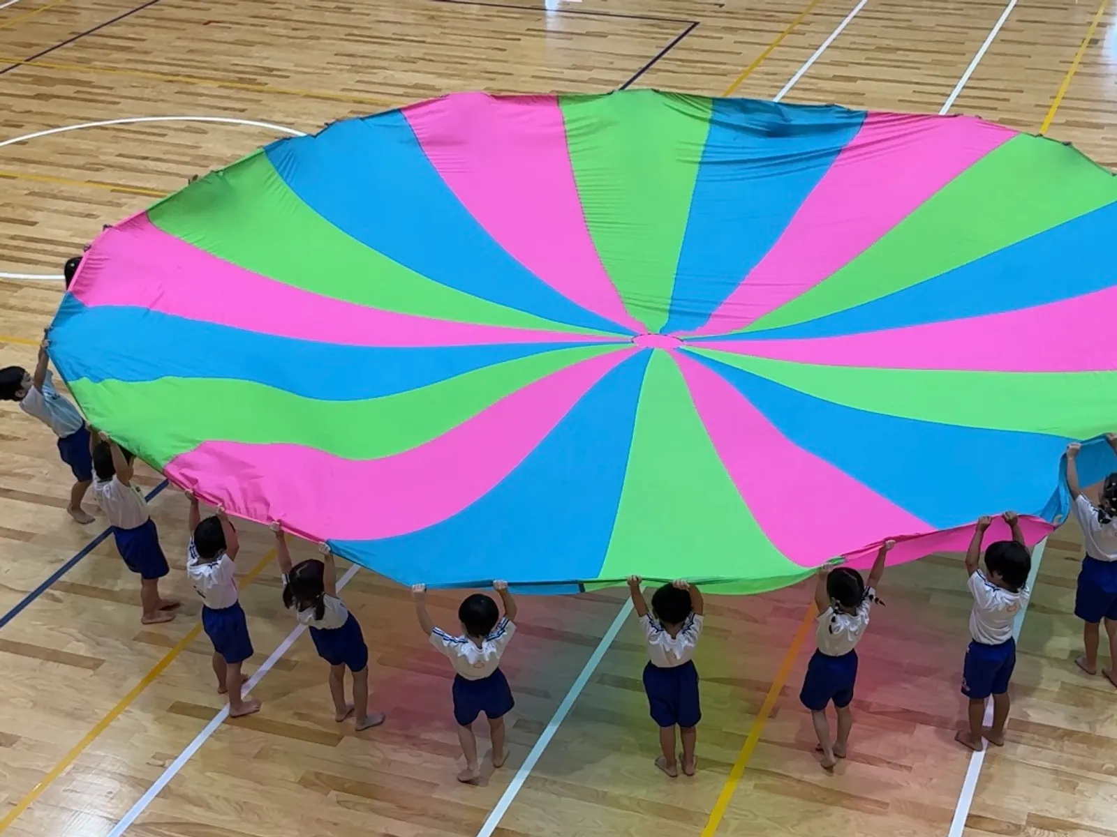運動会で大きなパラシュートを掲げる子どもたち（後ろ姿）